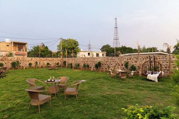 A grassy outdoor area with wicker furniture, a swing, and a stone wall.