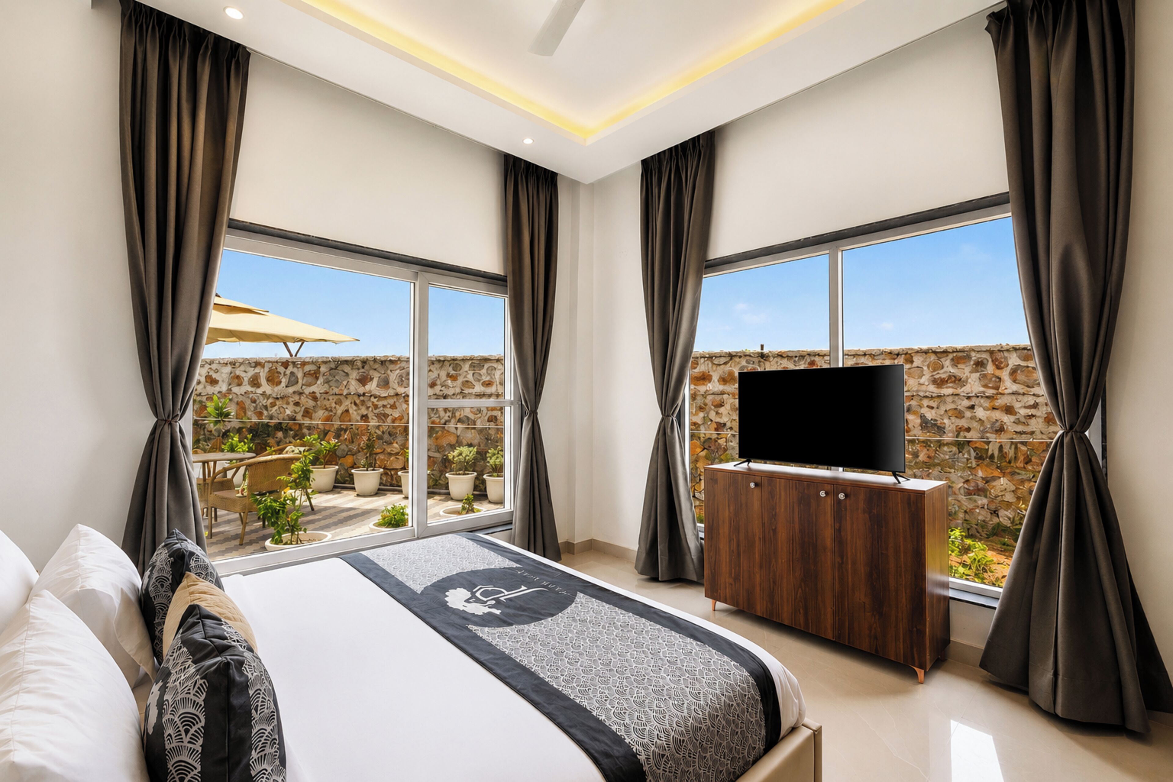 Ein modernes Schlafzimmer mit einem großen Bett, einem Flachbildfernseher und Blick auf eine Steinmauer sowie eine Sitzgelegenheit im Freien.