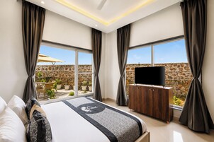 Une chambre moderne dotée d’un grand lit, d’un téléviseur à écran plat et offrant une vue sur un mur en pierre et un espace de détente extérieur.