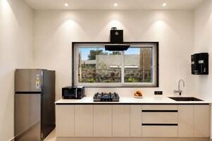 A modern kitchen with a built-in gas stove, a microwave, a refrigerator, and a window with a view of a stone wall and greenery.