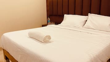 A neatly made bed with a rolled white towel, a wooden headboard, and a nightstand with a bottle and glasses.