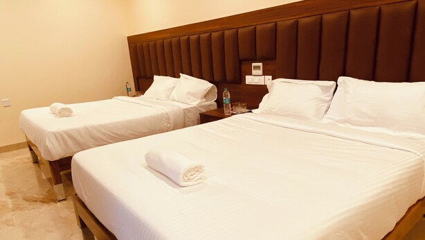 Two single beds with white linens and pillows, a wooden headboard, a nightstand with a water bottle and glasses, and a marble floor.