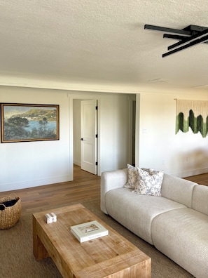A modern living room with a sofa, a coffee table with a book, a painting, and a door leading to another room.