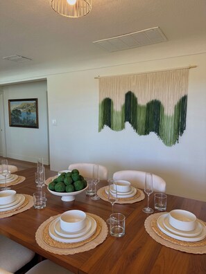 A dining room with a wooden table set for a meal, a decorative wall hanging, and a framed painting on the wall.