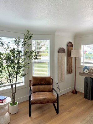 Une pièce avec un fauteuil en cuir, une plante en pot, une lampe et une fenêtre avec des stores.