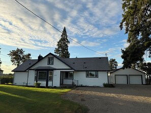 Une maison à deux étages avec un porche à l’avant, un garage et un ciel dégagé.
