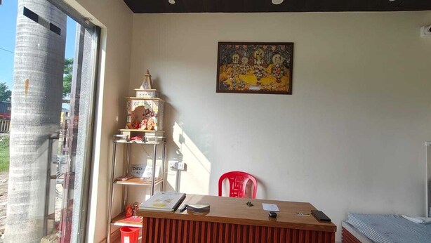 Een kamer met een receptiebalie, een rode stoel, een klein altaartje en een schilderij aan de muur.