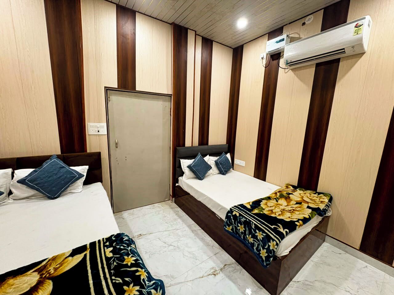 A hotel room with two beds, a wardrobe, an air conditioning unit, and a door.