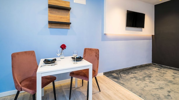 Ett modernt rum med ett vitt bord, två stolar, en platt-TV som är monterad på väggen och en hylla i trä.