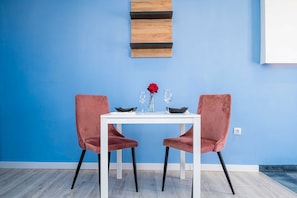 Ein Essbereich mit einem weißen Tisch, zwei rosafarbenen Stühlen und einer blauen Wand.