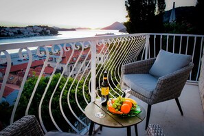 Ein Balkon mit einem Korbstuhl, einem kleinen Tisch mit Flasche und Gläsern sowie einer Obstschale.