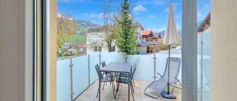 Un balcón con una mesa y sillas, una puerta de vidrio y vistas a una montaña y edificios.