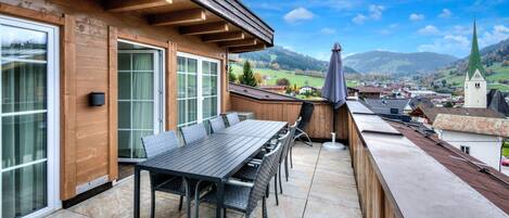 A terrace with a table and chairs, overlooking a town and mountains.