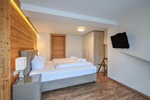 A modern hotel room with a bed, a flat-screen TV mounted on the wall, and a wooden accent wall. - Wildschonau Ski-in Brunner Apartment (Wildschönau)
