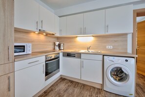 A modern kitchen with white cabinets, a built-in oven, microwave, dishwasher, and washing machine. - Wildschonau Ski-in Brunner Apartment (Wildschönau)