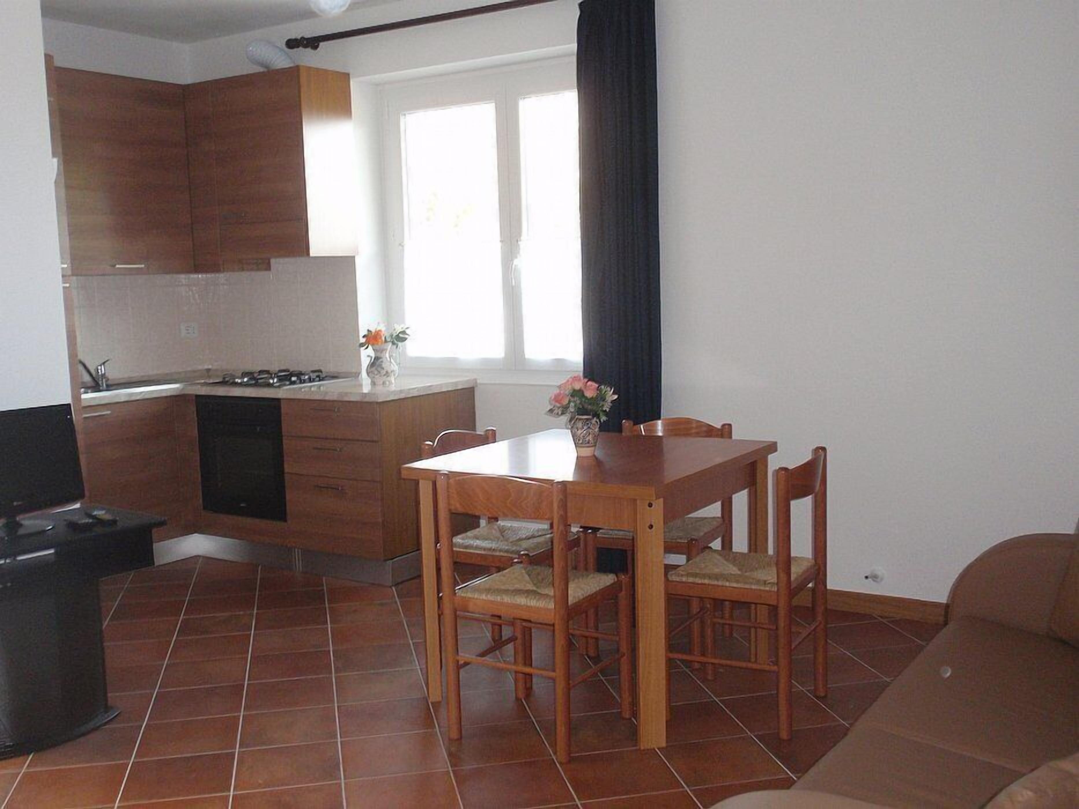 A compact kitchen with wooden cabinets, a dining table with chairs, and a black countertop.