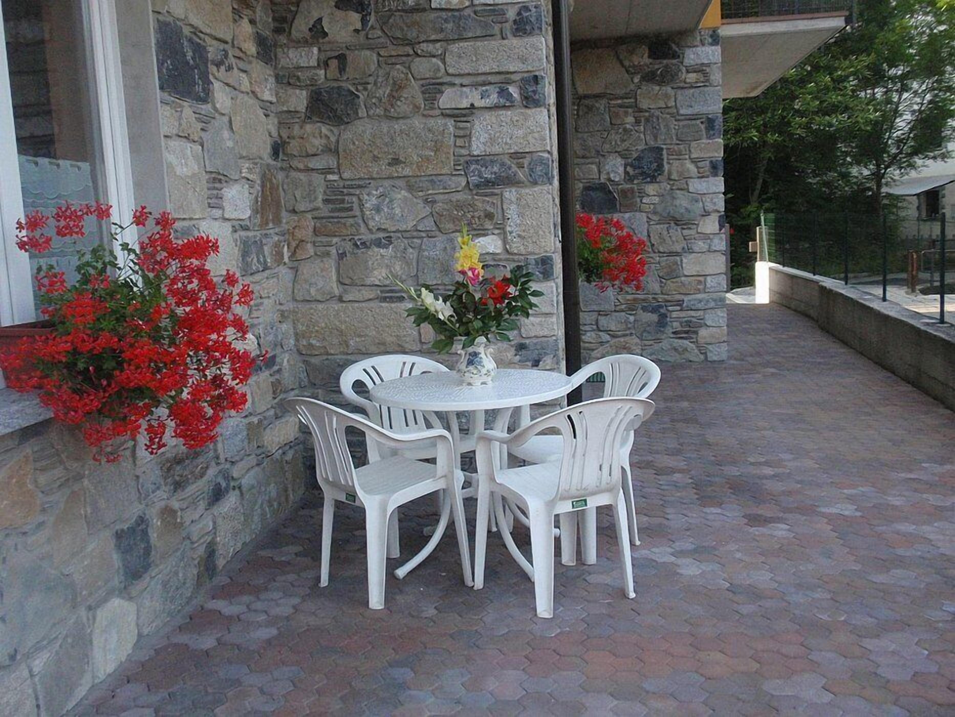 An outdoor patio with a stone wall, a round table, and four white chairs.