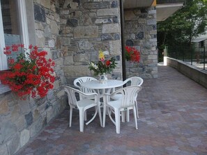 Eine Terrasse im Freien mit einer Steinsäule, einem runden Tisch und vier weißen Stühlen.