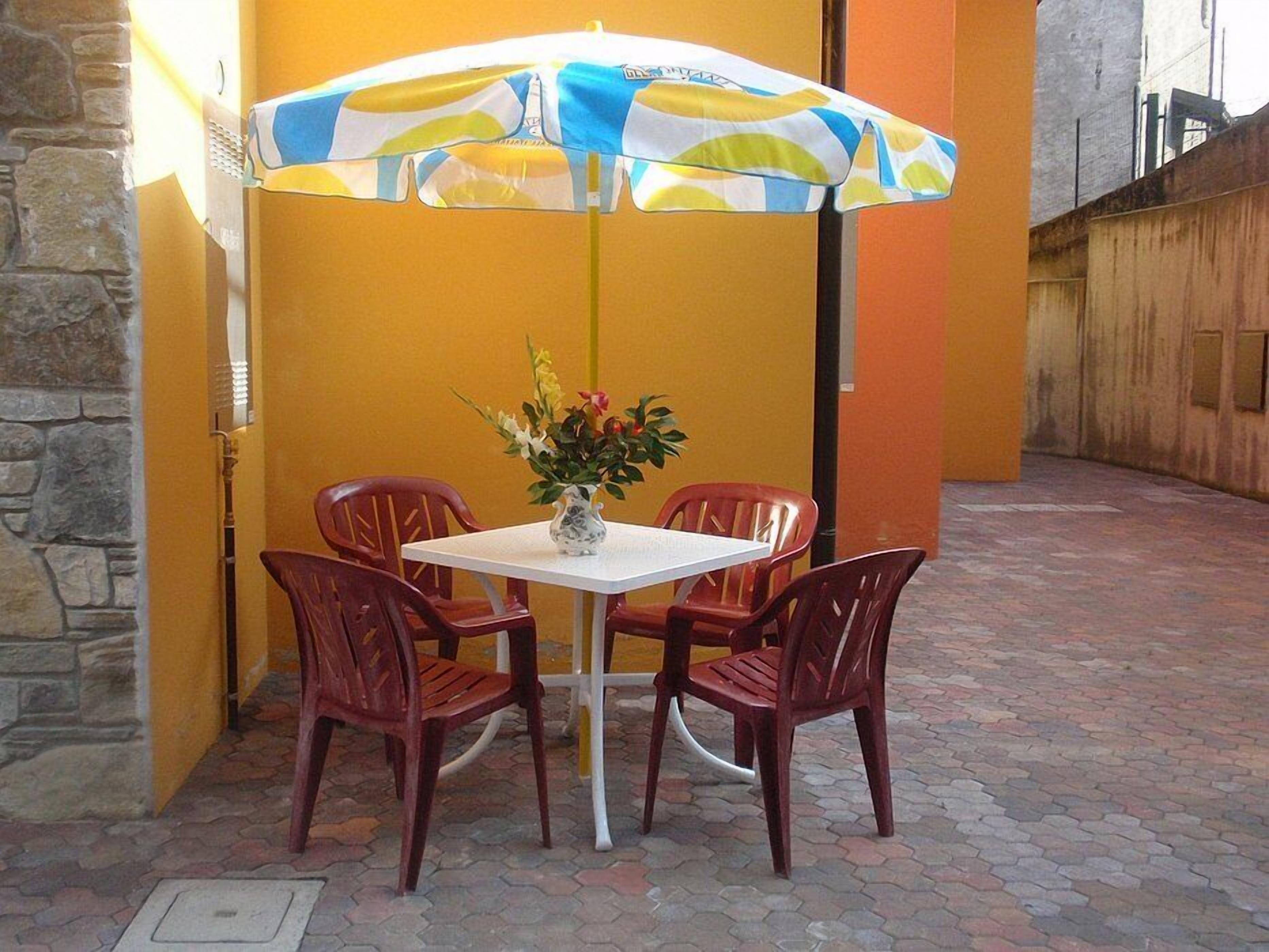 Un área de estar al aire libre con una mesa, sillas, una planta en maceta y un paraguas colorido.