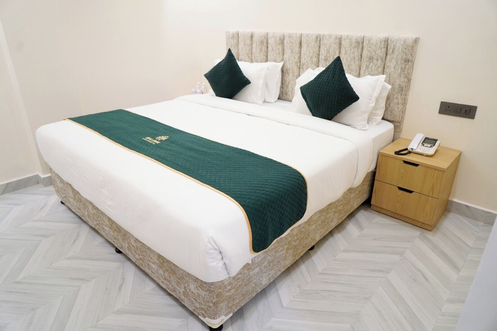 Habitación de hotel con cama, mesita de noche y toma de corriente.