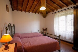 A bedroom with two beds, a wooden ceiling, a window with curtains, and a bedside table with a lamp. - Villa Angelisa Grande: A characteristic and welcoming three-story ancient tuscan country house surrounded by meadows and by green hills, with Free WI-FI. (Castiglion Fiorentino)