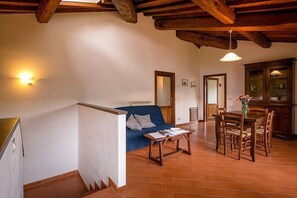 A spacious living area with a blue sofa, wooden dining table, and chairs. There is a staircase with a white railing leading to another level. - Villa Angelisa Grande: A characteristic and welcoming three-story ancient tuscan country house surrounded by meadows and by green hills, with Free WI-FI. (Castiglion Fiorentino)