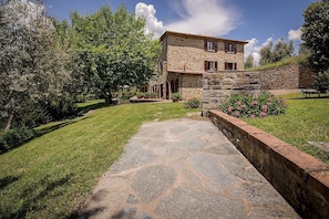 A stone house with a stone pathway leading to the entrance, surrounded by greenery and a clear sky. - Villa Angelisa Grande: A characteristic and welcoming three-story ancient tuscan country house surrounded by meadows and by green hills, with Free WI-FI. (Castiglion Fiorentino)
