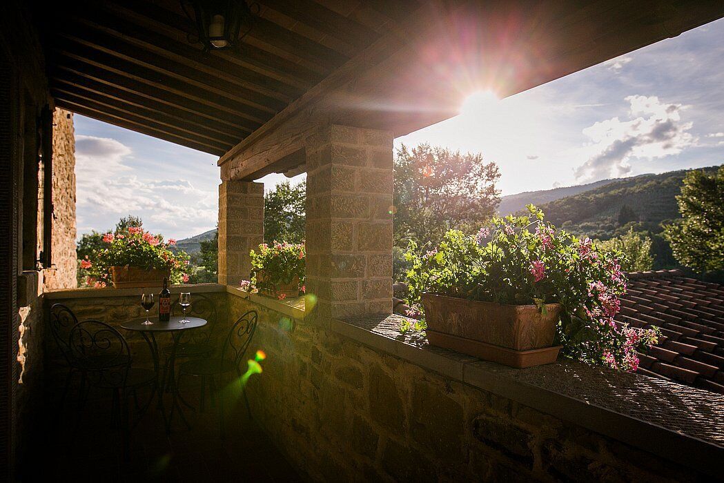 Un patio de piedra con una mesa y sillas, plantas en macetas y vistas a un paisaje montañoso.