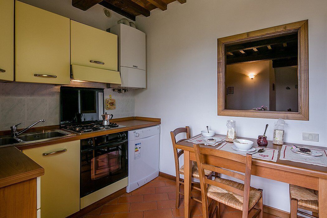 Una cocina compacta con estufa, pileta y lavavajillas pequeño. Cuenta con una mesa de comedor con sillas y un espejo colgante.