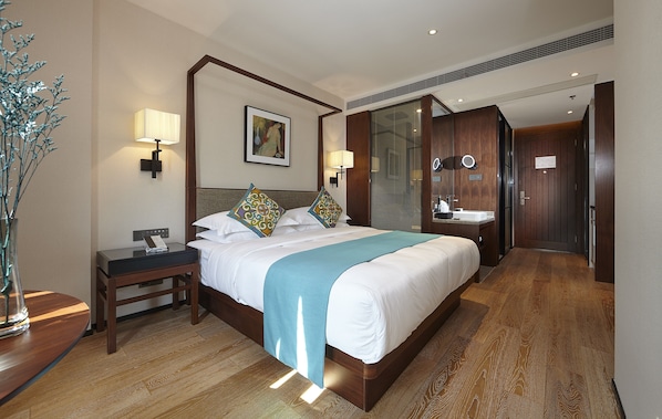 Une chambre d’hôtel avec un grand lit, des tables de chevet, une commode, un miroir, une salle de bain avec un lavabo et des toilettes, et un plancher en bois.