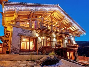 Una chalet in legno con balcone, fondamenta in pietra e luci a stringa.