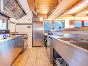 A modern kitchen with stainless steel appliances, wooden flooring, and a view of the mountains through the windows. - Chalet Farmhouse by Interhome (Villaroger)