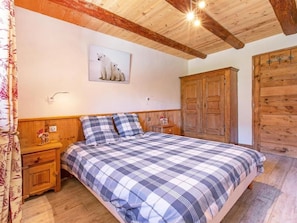 A bedroom with a checkered bedspread, wooden headboard, a nightstand, a wooden wardrobe, and a wall-mounted picture of polar bears. - Chalet Farmhouse by Interhome (Villaroger)