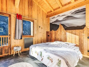 Camera da letto in una baita di legno con un letto, una finestra, un quadro e vista sulle montagne.
