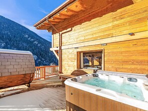Una baita di legno con vasca idromassaggio e terrazza con vista su una montagna innevata.