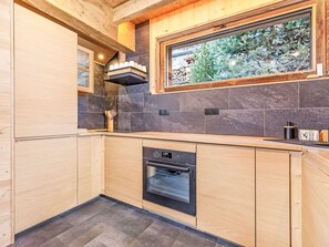 Eine moderne Küche mit Holzausstattung, einem eingebauten Ofen und einem Fenster mit Blick auf einen Garten.