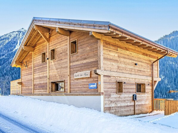 Una baita di legno con tetto spiovente, diverse finestre e un cartello che indica una località turistica in montagna.