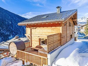 Una baita di legno con un balcone, un camino e vista su una montagna innevata.