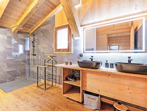 Ein modernes Badezimmer mit einem Holzlagerflächen, zwei großen Waschbecken, einer Duschkabine und einem Oberlicht.