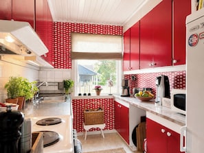 A kitchen with red cabinets, a window, and a view of a blue house outside.
