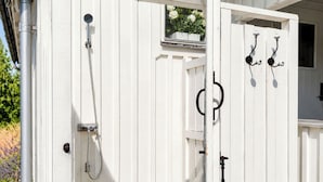A white wooden structure with a shower, a door, and a window with flowers.