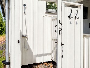 A white wooden structure with a shower, a door, and a window with flowers.