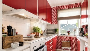 A kitchen with red cabinets, a white stove, and a window with a view of a house.