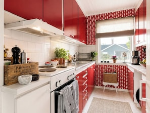 A kitchen with red cabinets, a white stove, and a window with a view of a house.