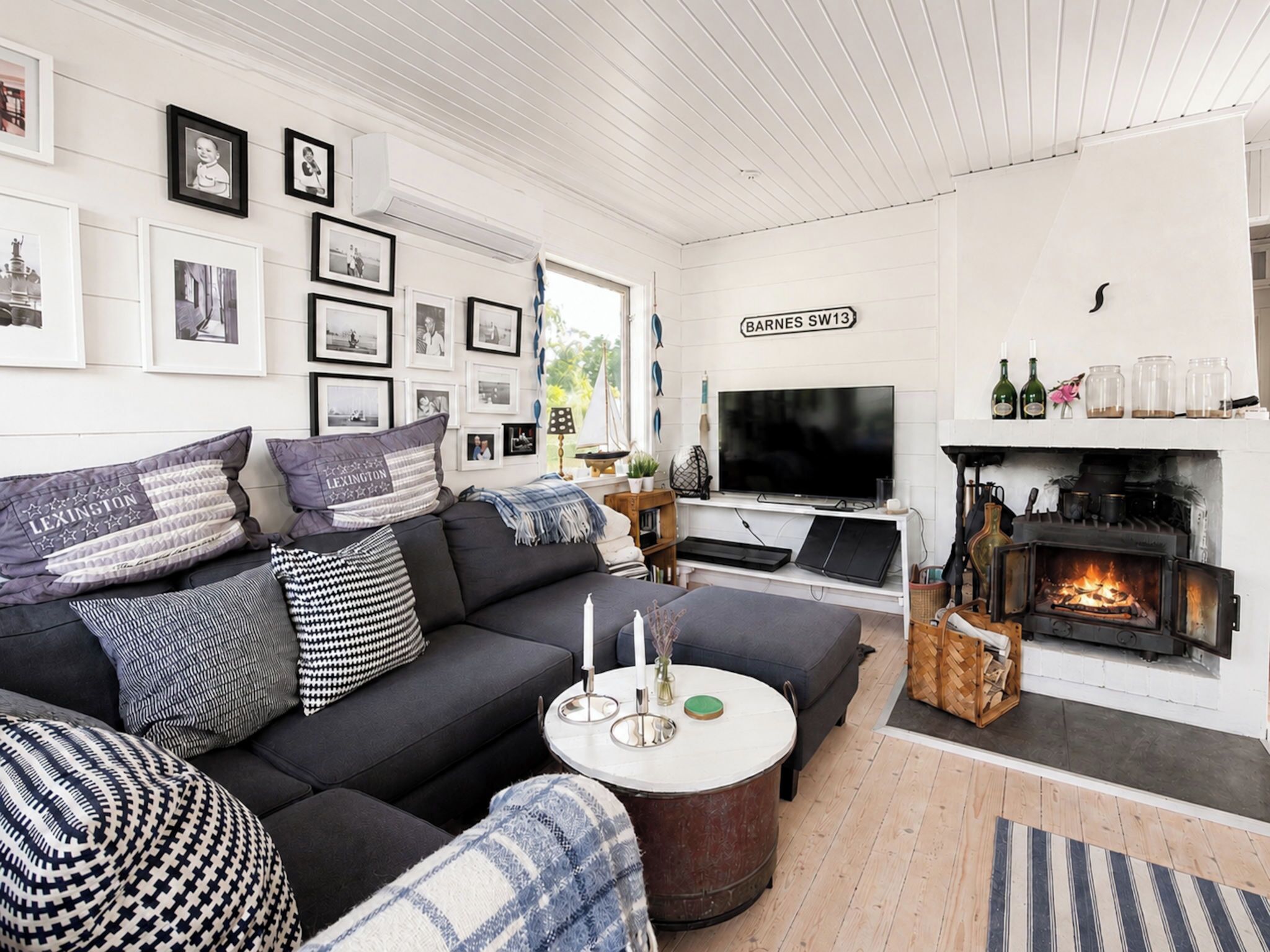 Una sala de estar moderna con un sofá negro, un televisor de pantalla plana, una chimenea y fotografías enmarcadas en la pared.