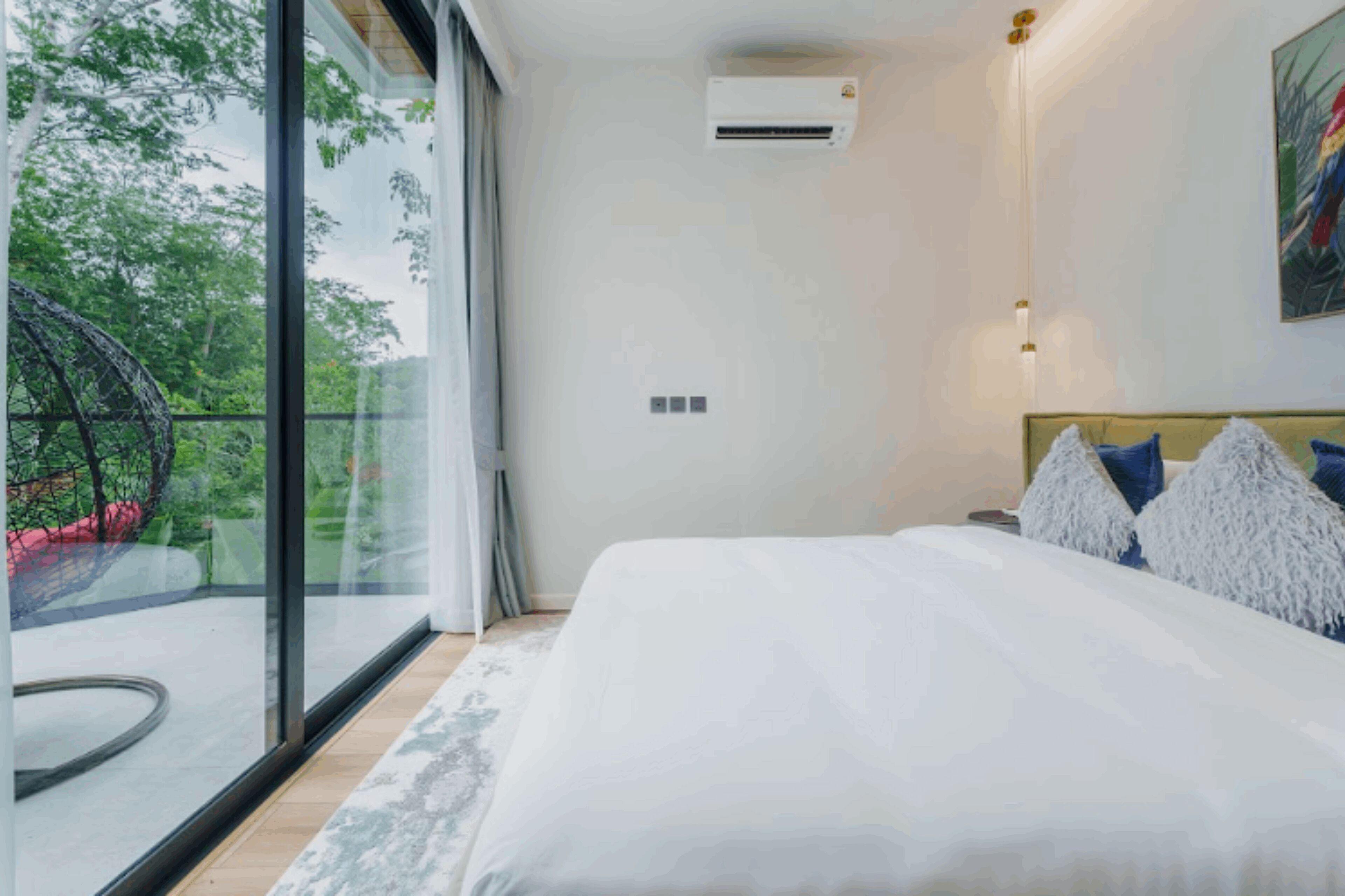 Une chambre dotée d’un grand lit, offrant une vue sur la verdure grâce à une porte coulissante, et d’un climatiseur fixé au mur.