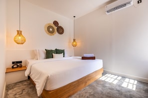 Un dormitorio con estructura de cama de madera, ropa de cama blanca, dos lámparas fijadas a la pared y una mesita de noche con una radio.