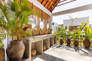 Un espacio exterior moderno con un banco de hormigón, plantas grandes en macetas y una pared de madera con espejos.
