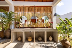 A concrete counter with three round mirrors, a bamboo curtain, and potted plants.