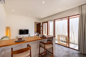 Una cocina moderna con una barra de madera, dos taburetes, un televisor de pantalla plana y un ventanal con vistas a bambú.